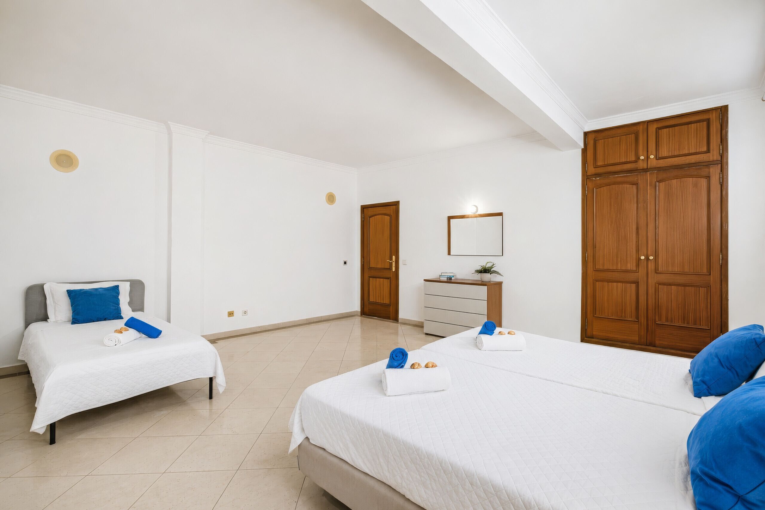 Une chambre d’hôtel avec deux lits, une armoire en bois, une table de chevet avec une lampe et une petite plante en pot.