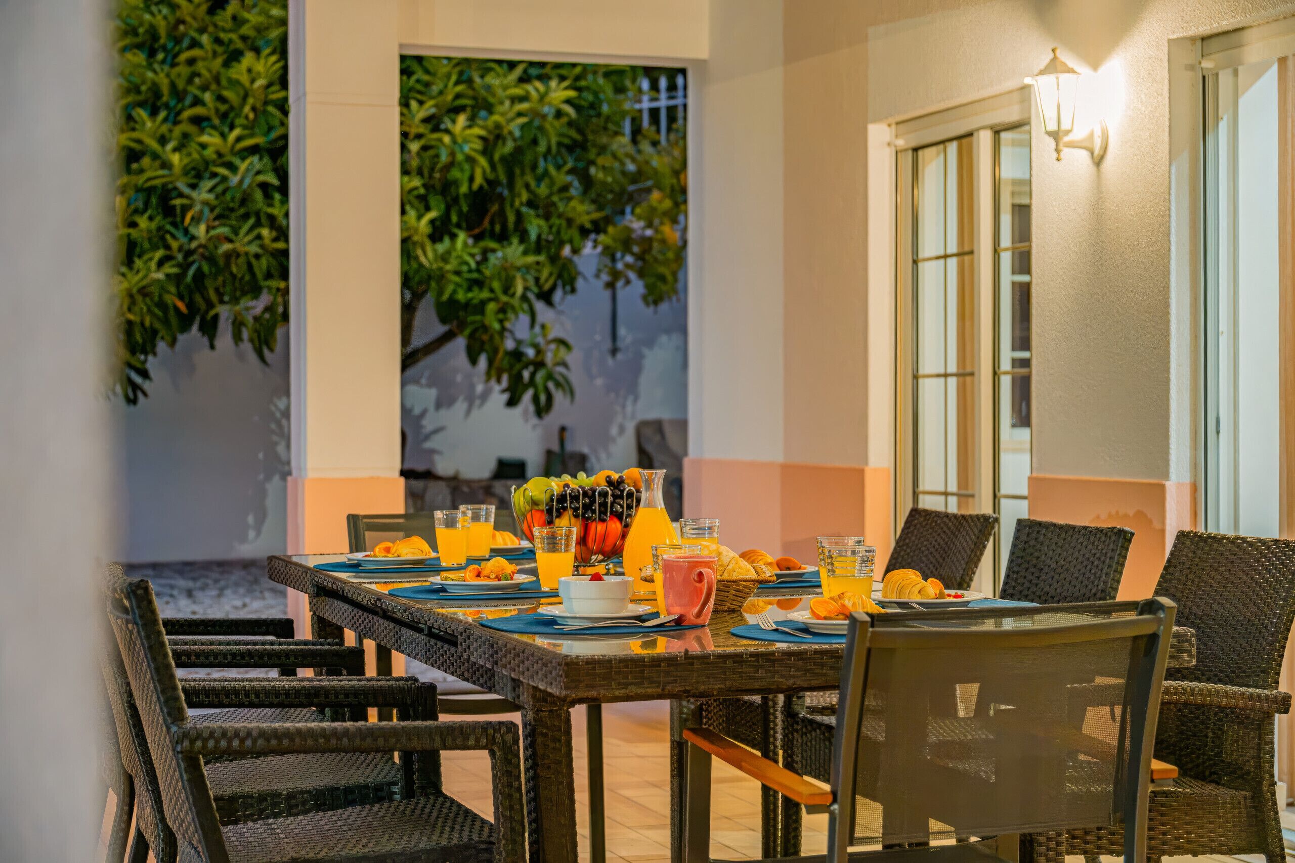 An outdoor dining area with wicker chairs and a table set for breakfast.