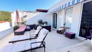Een terras op het dak met lounge stoelen, een tafeltje en potplanten.