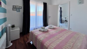 Een slaapkamer met een bed, nachtkastje, radiator, raam met gordijnen en een deur naar een andere kamer.