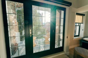 Een deur met een zwart frame en glazen ruit, met uitzicht op een bakstenen gebouw en een terras met rieten meubels.