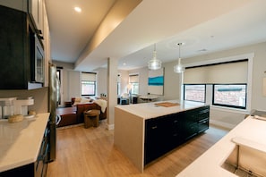 Een moderne keuken met een groot kookeiland, houten vloeren en een stadszicht door grote ramen.