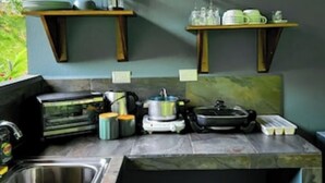 Cocina con encimera de mármol, un fregadero y diversos electrodomésticos. Dos estantes de madera sobre la encimera sostienen platos y vasos.