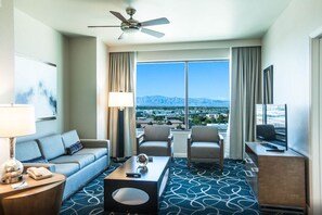Enjoy a mountain view from the large window in this stylish room, featuring a sofa, armchairs, and a desk with a lamp.
