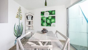Comedor con mesa y sillas de madera, una lámpara fijada a la pared y una obra de arte grande con temática de manzanas verdes.