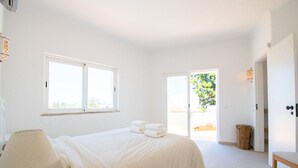 A bedroom with a bed, a lamp, a chair, and a door leading to a balcony. - Casa Pazovida - Walk to Carvoeiro, a perfect blend of convenience, comfort and luxury! (Carvoeiro)