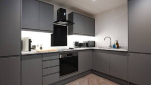 A modern kitchen with grey cabinetry, a black range hood, a built-in oven, a microwave, and a sink with a faucet.