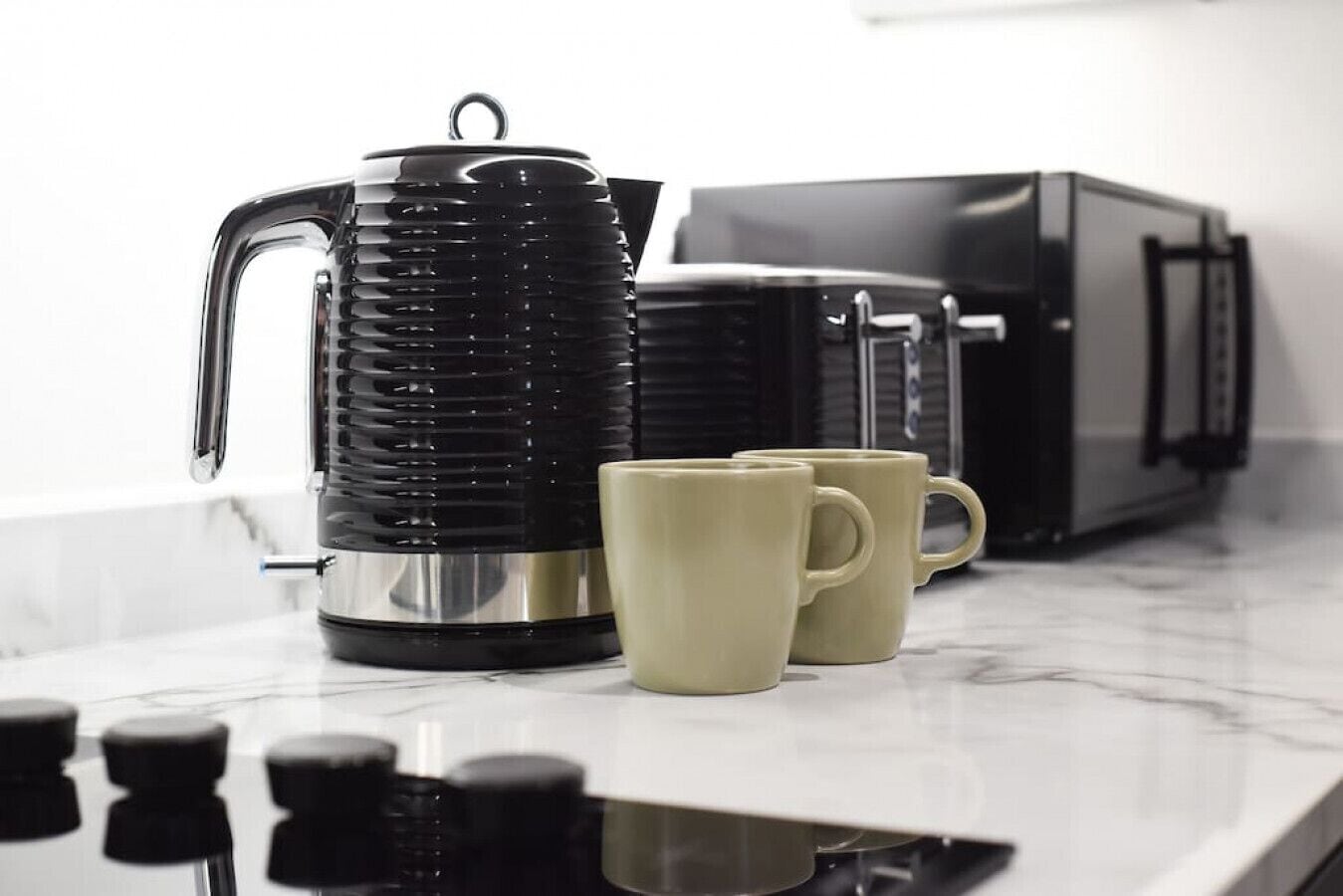 A kitchen with a black coffee maker, two beige mugs, and a toaster.