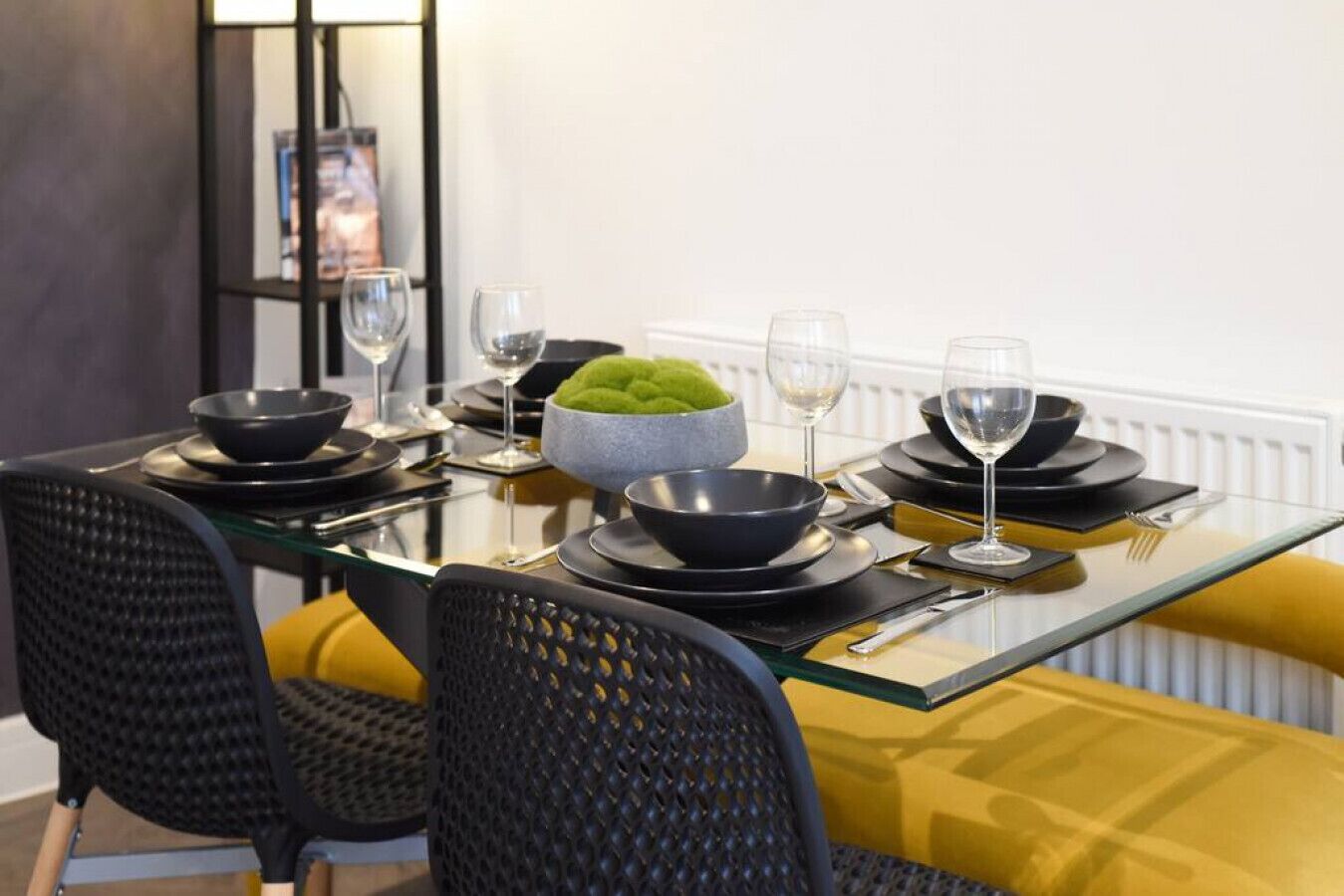 A dining table set with black bowls, wine glasses, and a green bowl centerpiece.