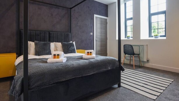 A modern bedroom with a four-poster bed, a glass desk, and a view of greenery outside.