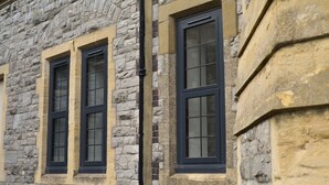 A stone building with three windows featuring dark frames and yellow window sills.