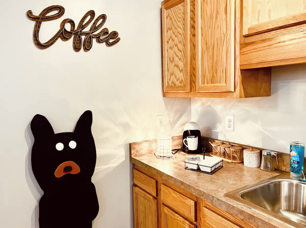 A kitchen with wooden cabinets, a coffee-themed wall decoration, a black bear decoration, and a coffee maker on the counter.