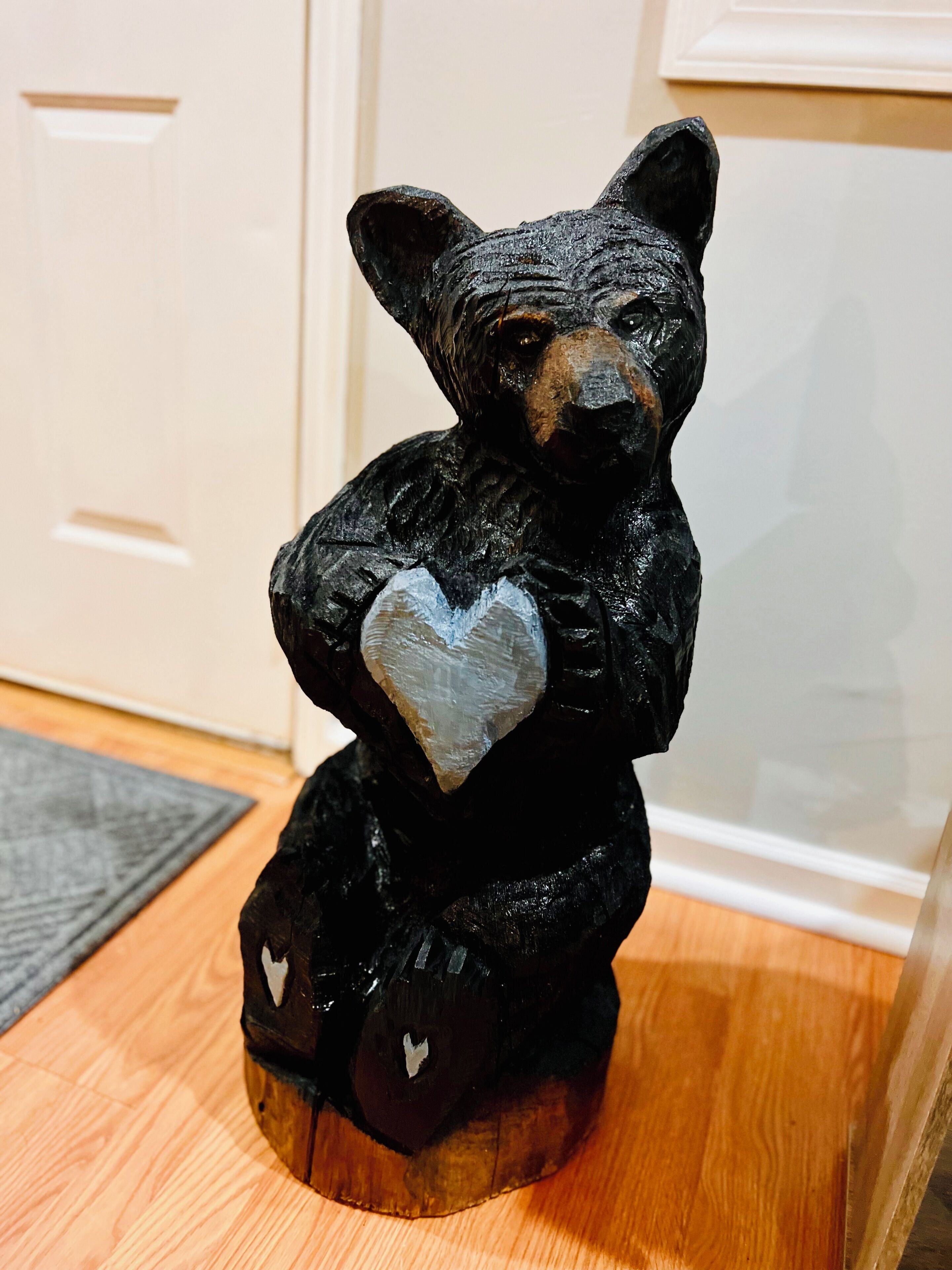A black bear figurine holding a heart on a wooden surface.