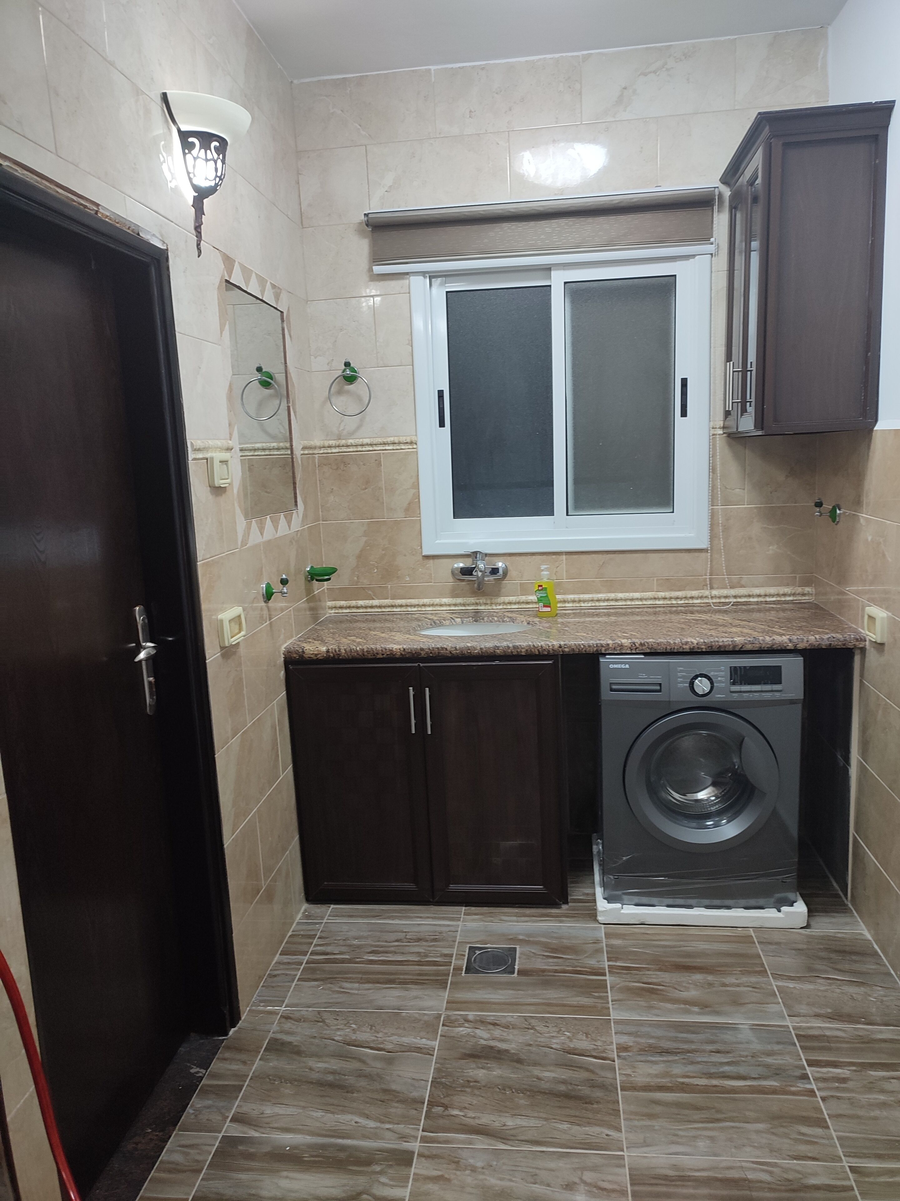 A compact kitchen with a built-in washing machine, a window above the sink, and a door with a handle.