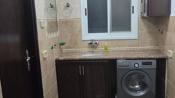 A compact kitchen with a built-in washing machine, a window above the sink, and a door with a handle.