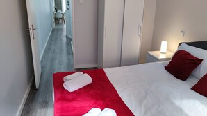 Ein Hotelzimmer mit Bett, Schrank, Nachttisch mit Lampe und einem zur Essecke führenden Gang.