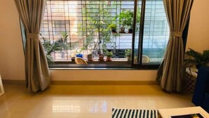 A room with a large window, curtains, and a tiled floor. - Nature Inspired Sun Drenched 1BR in Bandra (Mumbai)