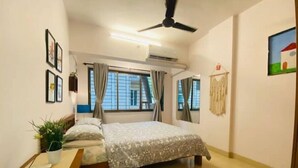 A bedroom with a bed, a desk, a plant, and a ceiling fan. - Nature Inspired Sun Drenched 1BR in Bandra (Mumbai)