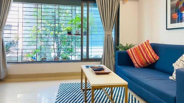 A living room with a sofa, a coffee table, and a window with curtains. - Nature Inspired Sun Drenched 1BR in Bandra (Mumbai)