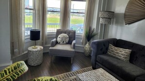 A corner living room with a grey sofa, a grey armchair with a decorative pillow, a round side table with a patterned top, and a floor lamp.