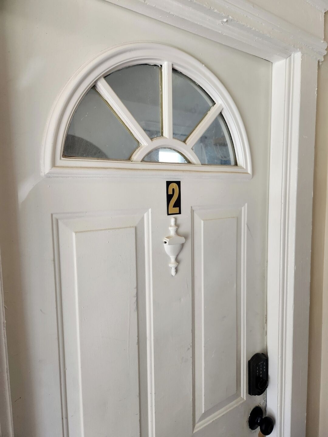 A white door with a number "2" sign, a window, and a doorbell.