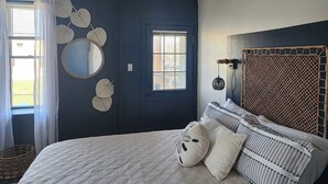 A bedroom with a dark blue door, a round mirror, and a bed with striped pillows.