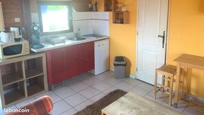 A compact kitchen with a microwave, toaster, and sink. There's a small trash bin and a wooden table with a chair. - Studio Meublé Pour Saisonnier (Auriolles)
