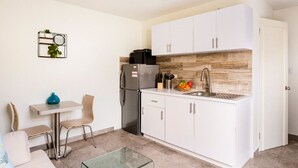 A compact kitchen with white cabinets, a stainless steel refrigerator, a sink, and a small dining area with a table and chairs.
