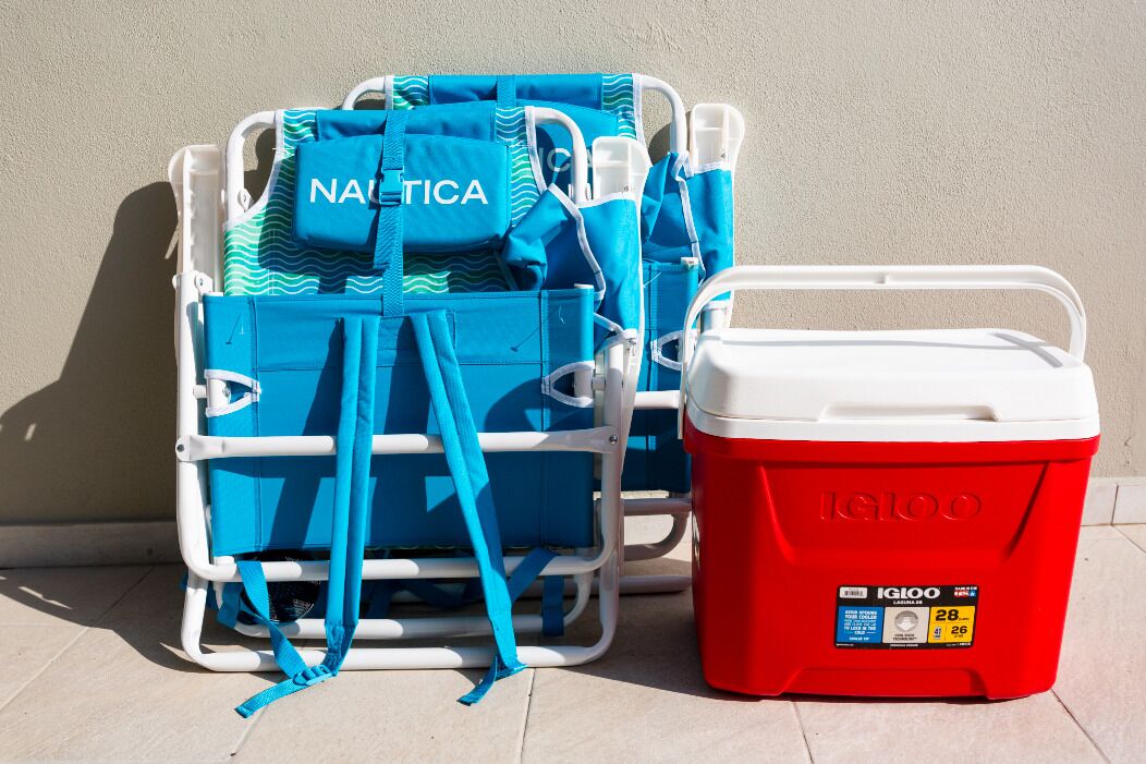 A beach chair cart with blue beach towels and a red Igloo cooler.