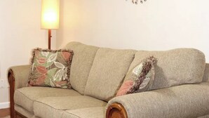 Een beige bank met bloemenkussens en een wandlamp.