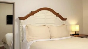 Een bed met een houten hoofdbord, een nachtkastje met een lamp en een spiegel aan de muur.