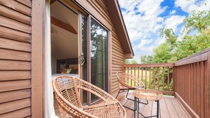 A wooden deck with wicker chairs and a table, a sliding glass door leading to an interior room, and a wooden fence surrounding the deck.