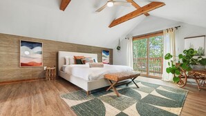 A bedroom with a large bed, wooden beams, a ceiling fan, and a view of the outdoors.