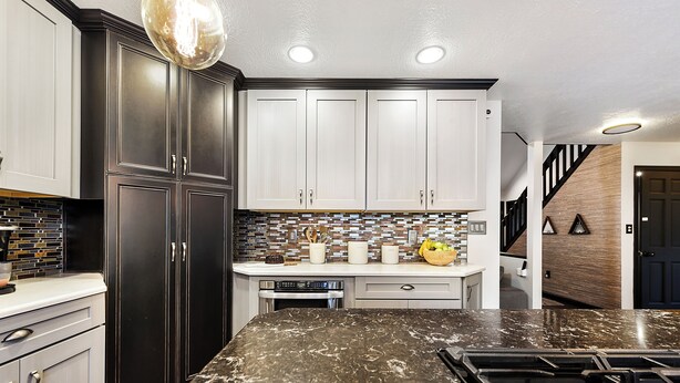 A modern kitchen with dark cabinets, a marble countertop, and a built-in stove.