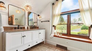 A bathroom with a large vanity, two mirrors, and a window with curtains.