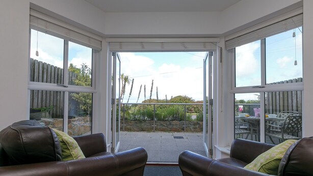 A sunlit room with a glass door leading to an outdoor patio area, furnished with leather sofas and a dining table. - 2 Four Seasons (St Ives)