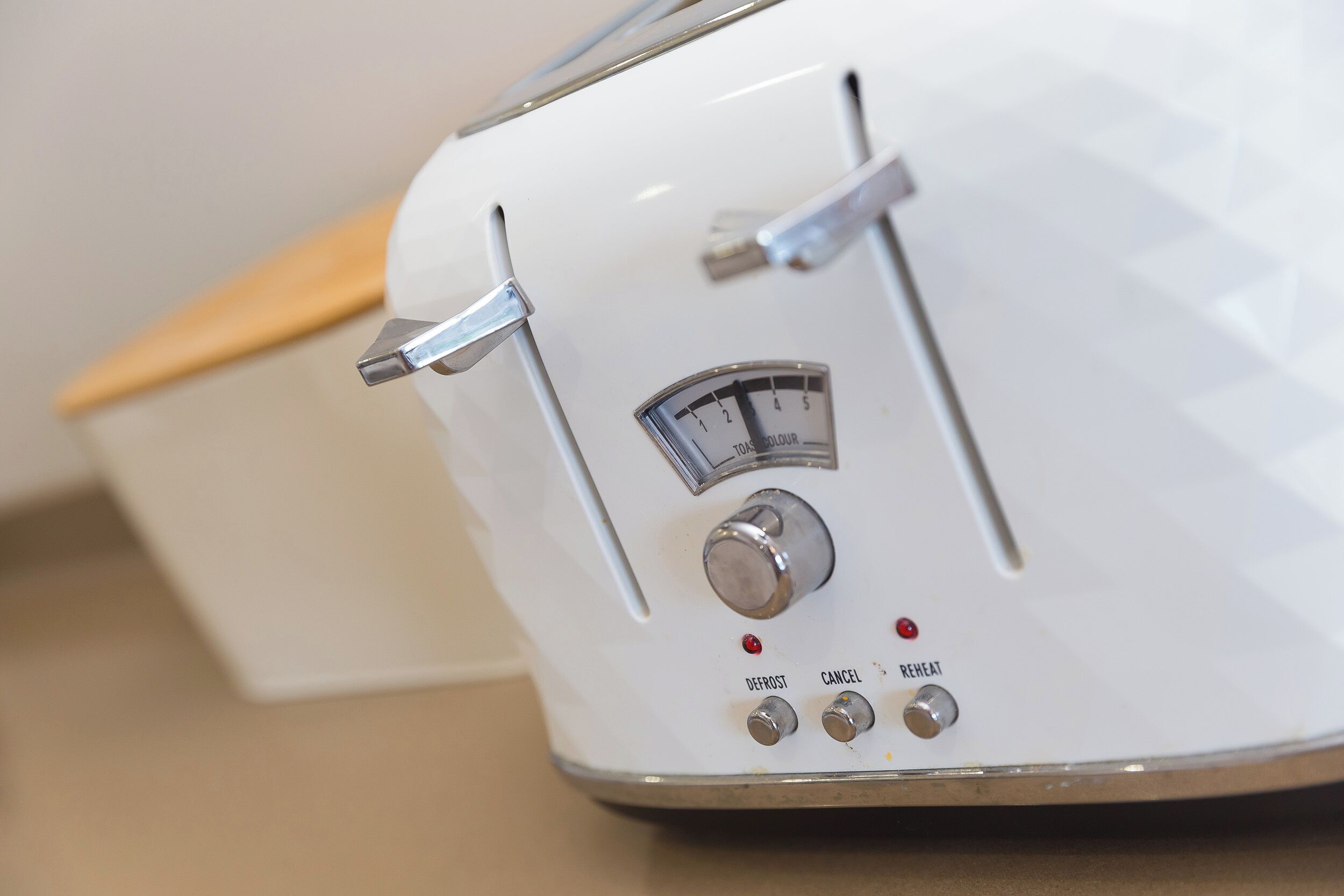 A white toaster with a dial and buttons labeled "DEFROST," "CANCEL," and "REHEAT."