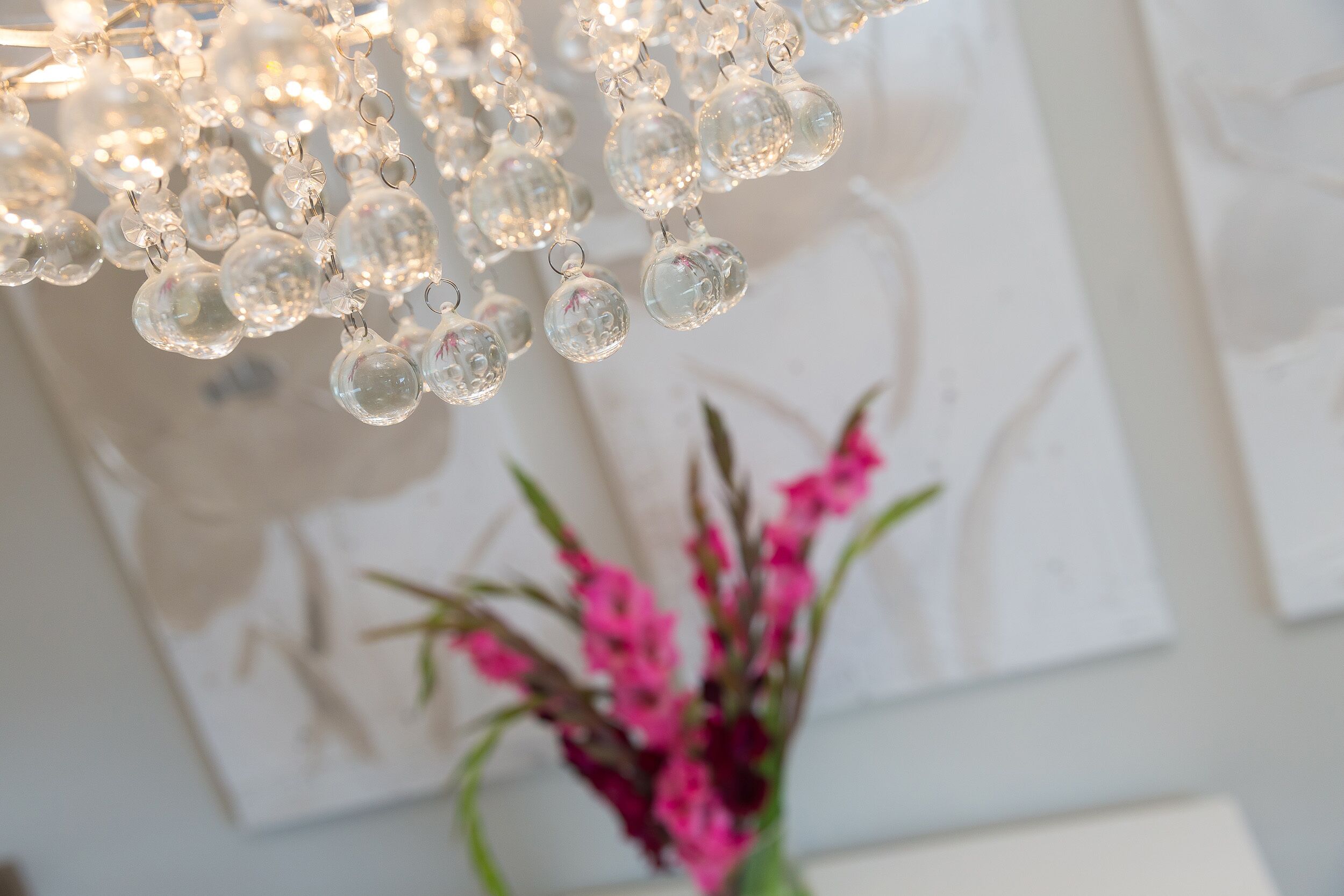 A chandelier with clear glass orbs and a vase with pink flowers.