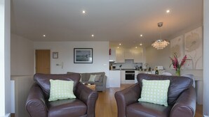 A living room with two leather armchairs, a sofa, a dining area, and a kitchen in the background. - 2 Four Seasons (St Ives)