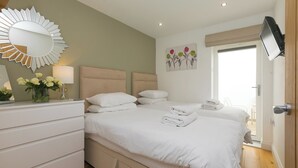 A bedroom with a bed, bedside tables, a mirror, a wall-mounted TV, and a door leading to a balcony. - 2 Four Seasons (St Ives)