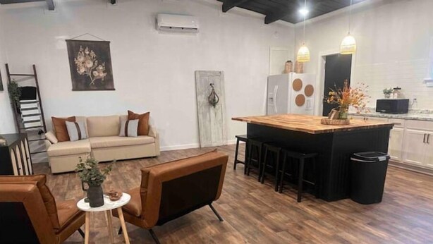Un espace de vie moderne comprenant un canapé, deux fauteuils, une petite table ronde et un coin cuisine avec un comptoir-bar.