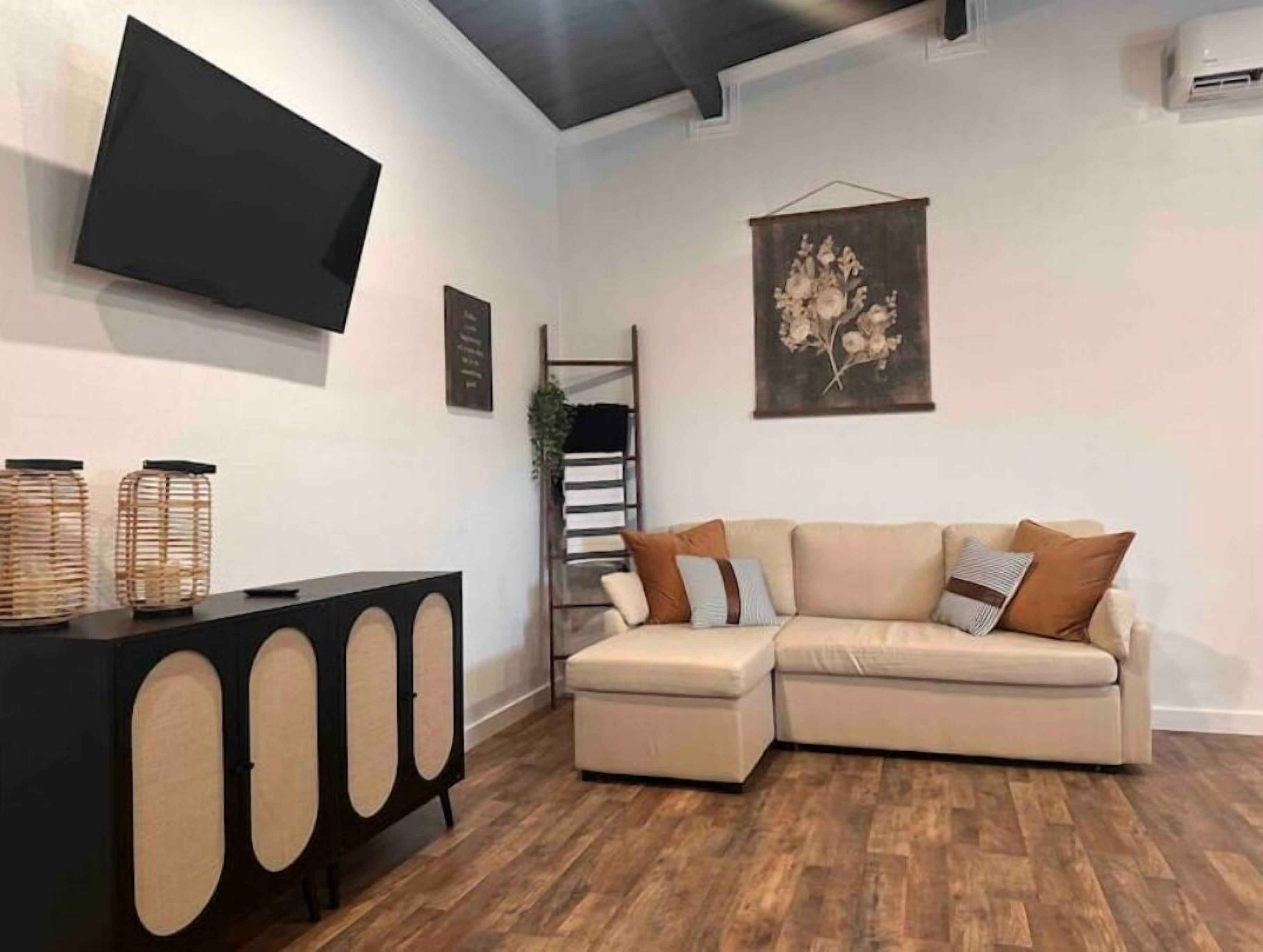 A living room with a sectional sofa, a black console table with circular cutouts, a flat-screen TV mounted on the wall, and a wooden floor.