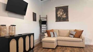 A living room with a sectional sofa, a black console table with circular cutouts, a flat-screen TV mounted on the wall, and a wooden floor.