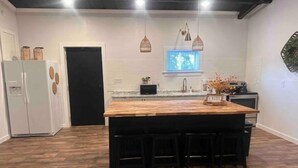 Une cuisine dotée d’un grand îlot central en bois, de tabourets de bar noirs, d’une porte noire et de luminaires suspendus.