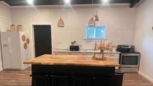 Une cuisine avec un îlot central en bois, des tabourets de bar noirs, un réfrigérateur, un four à micro-ondes et une fenêtre donnant sur un beau paysage.