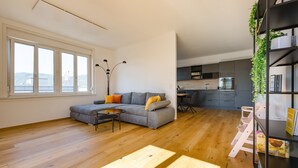A modern living room with a grey sofa, wooden flooring, and a view of the kitchen. - Tamlivingcenterluxus4 Zimmer mit Smart Tvküche (Graz)