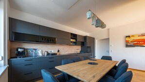 A modern kitchen with dark cabinets, a wooden dining table, and blue chairs. - Tamlivingcenterluxus4 Zimmer mit Smart Tvküche (Graz)
