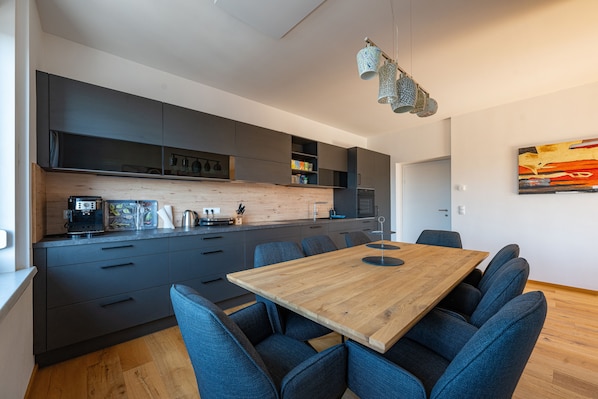 A modern kitchen with dark cabinets, a wooden dining table, and blue chairs.