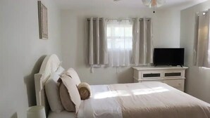 Un dormitori amb un llit, televisió, una taula de nit i una finestra amb cortines.