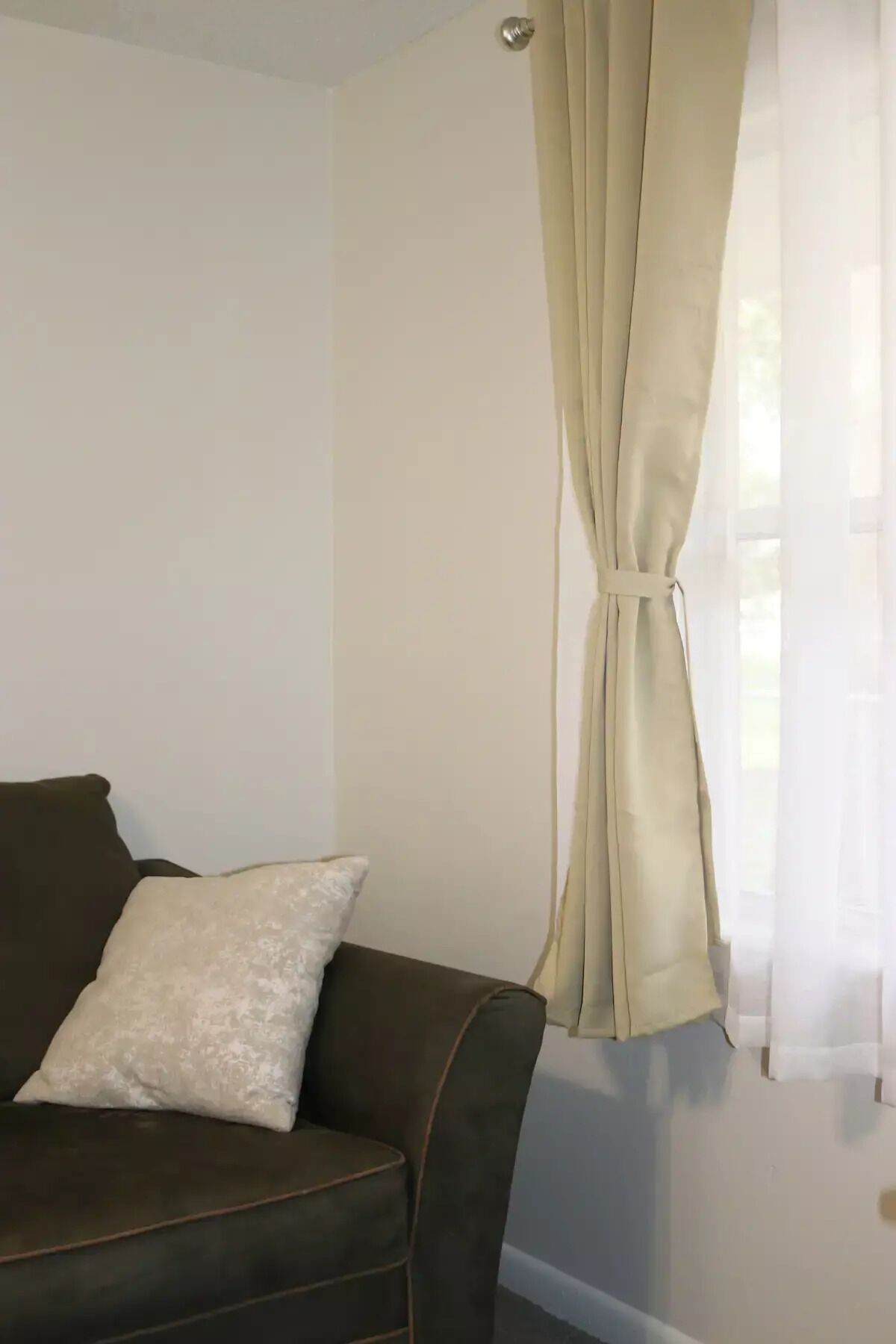 Una sala de estar con un sofá marrón, un cojín blanco y una cortina color beige.